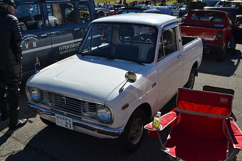 White small pickup with a red folding chair beside it in a busy car park. Opens a larger view