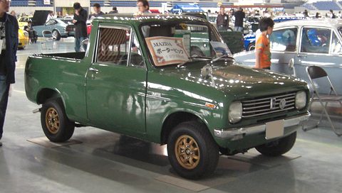 Dark green small pickup with gold wheels on a hall floor, a sign on its windscreen. Opens a larger view
