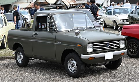 Dark grey-green small pickup on gravel, visitors and cars behind. Opens a larger view
