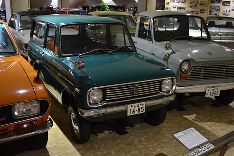 Dark teal small van with a chrome grille between an orange car and a white pickup. Opens a larger view