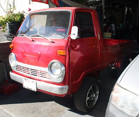 Red cab-over pickup with alloy wheels parked in a carport. Opens a larger view