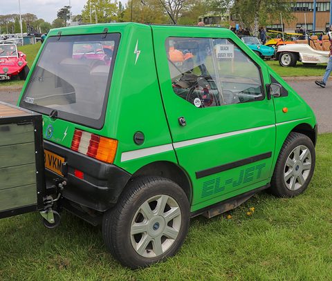 Rear of a bright green angular microcar with a glass hatch, EL-JET lettering and a small trailer attached. Opens a larger view