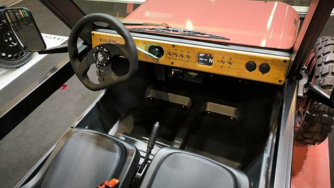 Wooden dashboard panel with a small display, a three-spoke wheel and two black seats in an open body. Opens a larger view