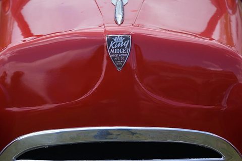 Shield badge with a crown and the words King Midget, Midget Motors Mfg. Co., Athens, Ohio, under a chrome bonnet mascot on red paint. Opens a larger view