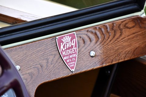 Maroon shield badge reading King Midget, Midget Motors Mfg. Co., fixed to varnished oak beneath a black screen frame. Opens a larger view