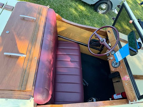 Looking down into a small open car: maroon bench seat, purple steering wheel, wooden rear deck and door panels, and a blue ribbon on the dash. Opens a larger view