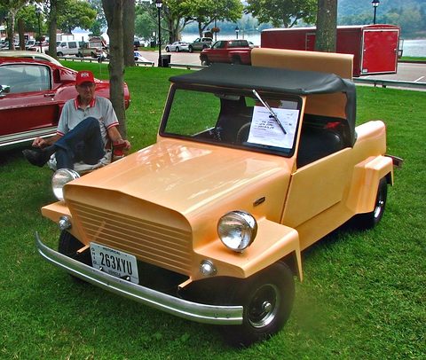 A small tan open utility car with a slatted grille, twin headlamps and a chrome bumper, its owner seated behind. Opens a larger view