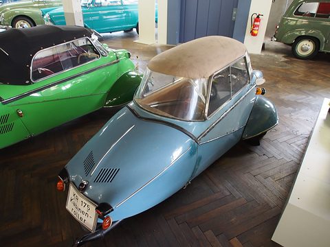 Tapering pale blue tail with louvres and a single rear wheel, green cars beside it. Opens a larger view