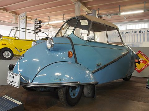 Pale blue tandem two-seater with enclosed front wings and a beige fabric roof on a parquet floor. Opens a larger view