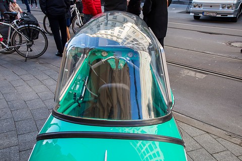 Clear plastic dome over a turquoise tandem cockpit, reflecting the building opposite. Opens a larger view