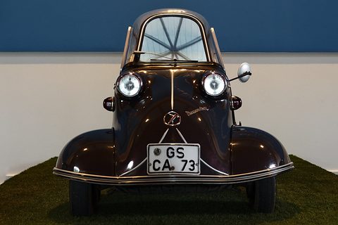 Dark brown bubble car facing the camera on a grass mat, plate GS-CA 73. Opens a larger view