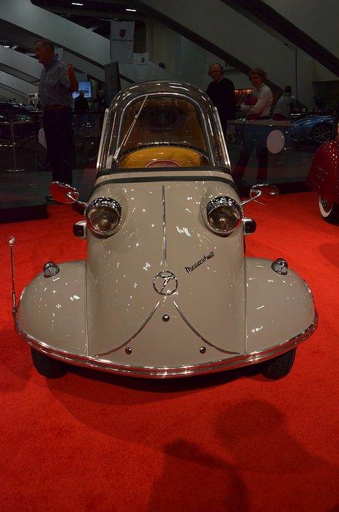 Grey bubble car head-on on red carpet, visitors in the background. Opens a larger view