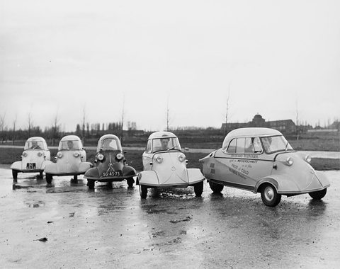 Black-and-white photograph of five Messerschmitt cabin scooters lined up on a wet quay