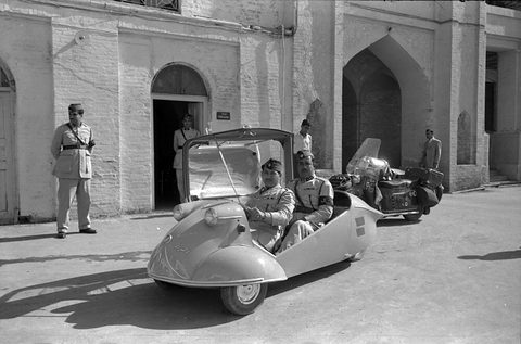 Two men in uniform sit in an open tandem bubble car by a doorway, another officer standing. Opens a larger view