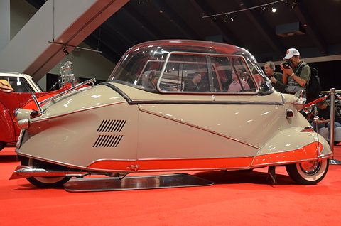 Grey tandem bubble car with red lower trim side-on on red carpet, a photographer behind. Opens a larger view