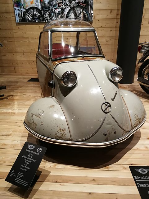 Weathered grey nose with two headlamps, a black museum sign on a stand beside it. Opens a larger view