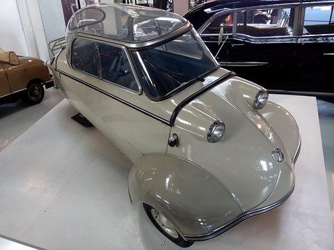 Grey bubble car with clear canopy on a white plinth in a museum hall. Opens a larger view