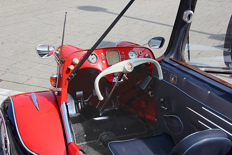 Looking down into a red KR200 cockpit: a cream steering bar, a round speedometer and the driver’s seat. Opens a larger view