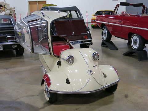 A cream three-wheeled bubble car with whitewall tyres and red upholstery, its clear canopy swung open to the side. Opens a larger view