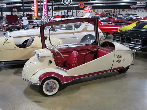 Side view of a cream three-wheeler with a maroon sweep, red tandem seats and an open canopy, neon signs behind. Opens a larger view