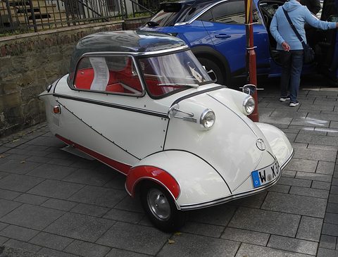 White bubble car with red lower panels on paving, registration W-X 33. Opens a larger view