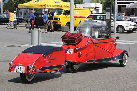 A red KR200 from behind, a suitcase strapped to its rack and a little trailer hitched to the tail. Opens a larger view