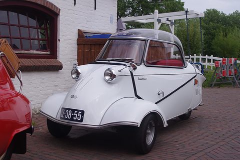 White bubble car on red brick paving beside a whitewashed building. Opens a larger view