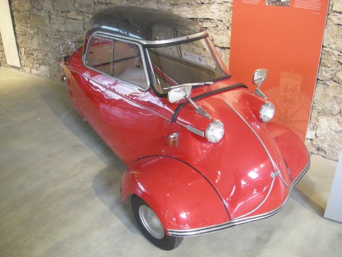 Red bubble car with clear canopy and mirrors against a stone wall. Opens a larger view