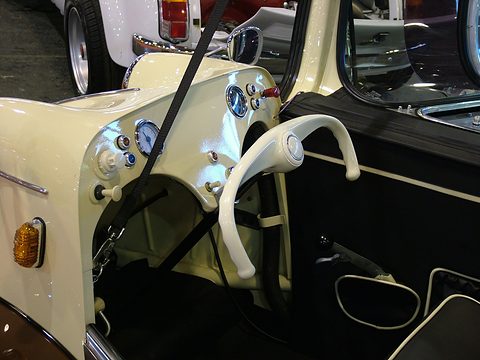 Cream handlebar and dashboard with blue-ringed dials beside a dark interior. Opens a larger view
