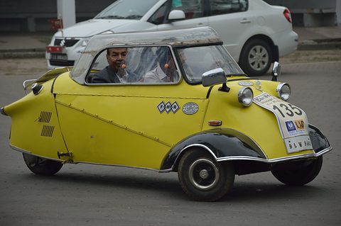Yellow bubble car with rally number 135 on the move, its driver visible through the canopy. Opens a larger view