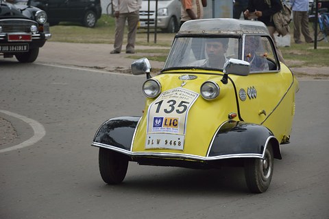 Yellow bubble car with black wings and a rally plate approaching on a road. Opens a larger view