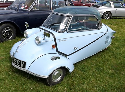 Pale blue bubble car with registration SEV on grass beside a dark saloon. Opens a larger view