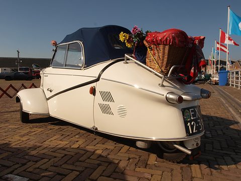 White tapering tail with a wicker basket on the rear rack, flags flying on the quay behind. Opens a larger view