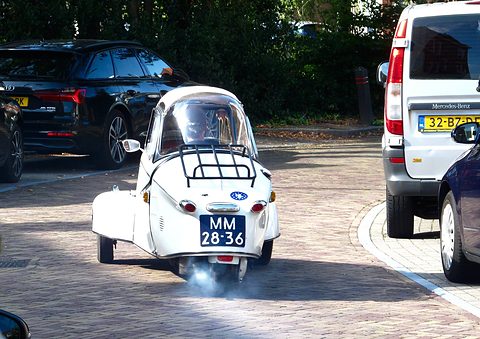 White bubble car from behind with chrome rack, plate MM-28-36, blue exhaust smoke at the tail. Opens a larger view