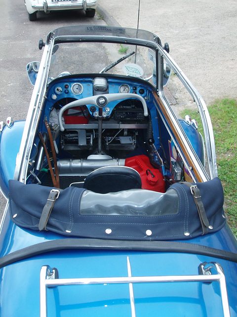 Blue tandem cockpit from behind: two seats, handlebar and dashboard beneath the raised canopy. Opens a larger view