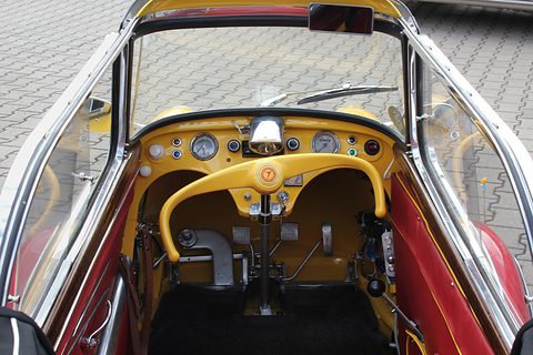 The cockpit of a yellow KR200 Cabrio-Limousine seen from behind: the yellow steering bar, a row of dials and the two seats. Opens a larger view