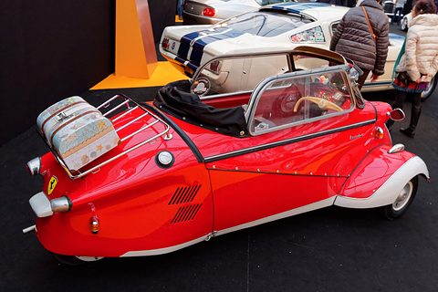 Red tapering tail with a luggage rack and suitcase, visitors at the edge of the stand. Opens a larger view