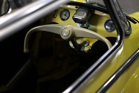 Cream handlebar steering in front of a yellow dashboard with a speedometer, seen through the canopy frame. Opens a larger view