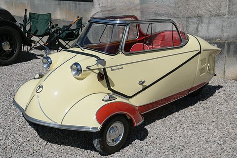Cream three-wheeler with red wheel arches and a dark-framed canopy on gravel. Opens a larger view