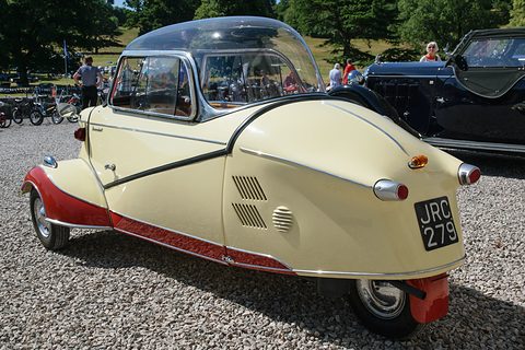 Cream tapering tail with louvres and red lower trim on gravel, trees behind. Opens a larger view