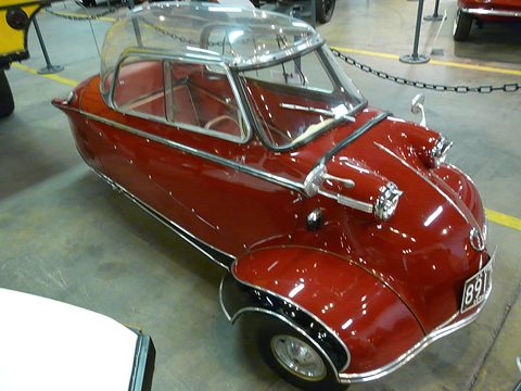 Maroon bubble car with clear canopy and chrome trim behind a chain barrier. Opens a larger view