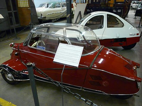 Maroon tandem bubble car side-on, an information sheet on its canopy, a white car behind. Opens a larger view
