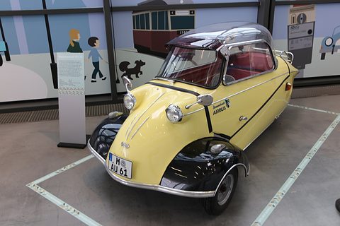 Yellow bubble car with black wings and Airbus lettering, registration M-AU 61, on a hall floor. Opens a larger view