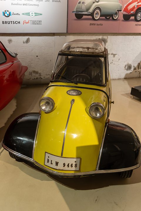 Yellow bubble car with black front wings and registration DLW 9468, a museum poster behind. Opens a larger view