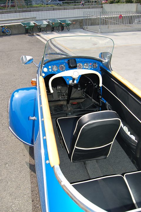 Looking down into an open blue body at a handlebar, dashboard and two black seats in line. Opens a larger view