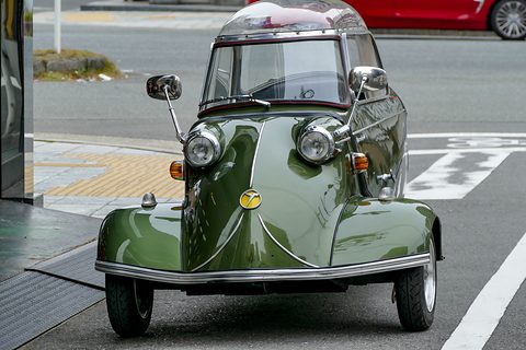 Dark green bubble car head-on on a street with road markings behind. Opens a larger view