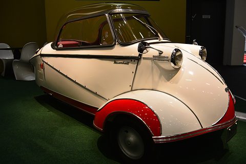 White bubble car with red wings on a dark show stand, canopy closed. Opens a larger view
