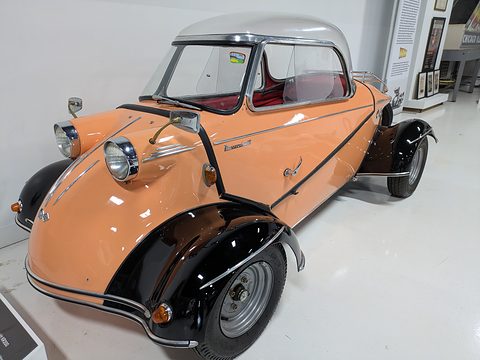 Orange bubble car with black wings and red interior on a white floor. Opens a larger view
