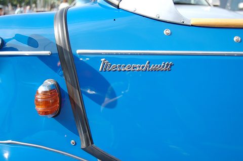 Close-up of a chrome Messerschmitt script badge on a blue body beside an orange indicator lens. Opens a larger view
