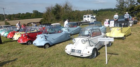 A row of bubble cars in many colours across a field, a white one in front.